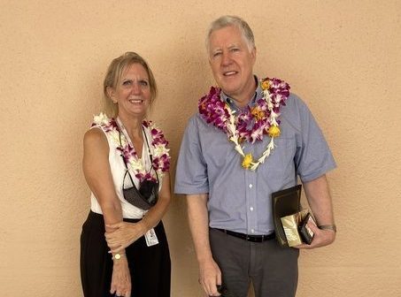 A man and a woman wearing lei and holding awards